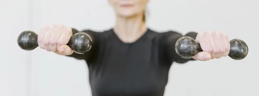 Exercice de Pilates au sol avec petites haltères pour renforcer les bras, les épaules et le haut du corps tout en travaillant la stabilité et le contrôle du mouvement.